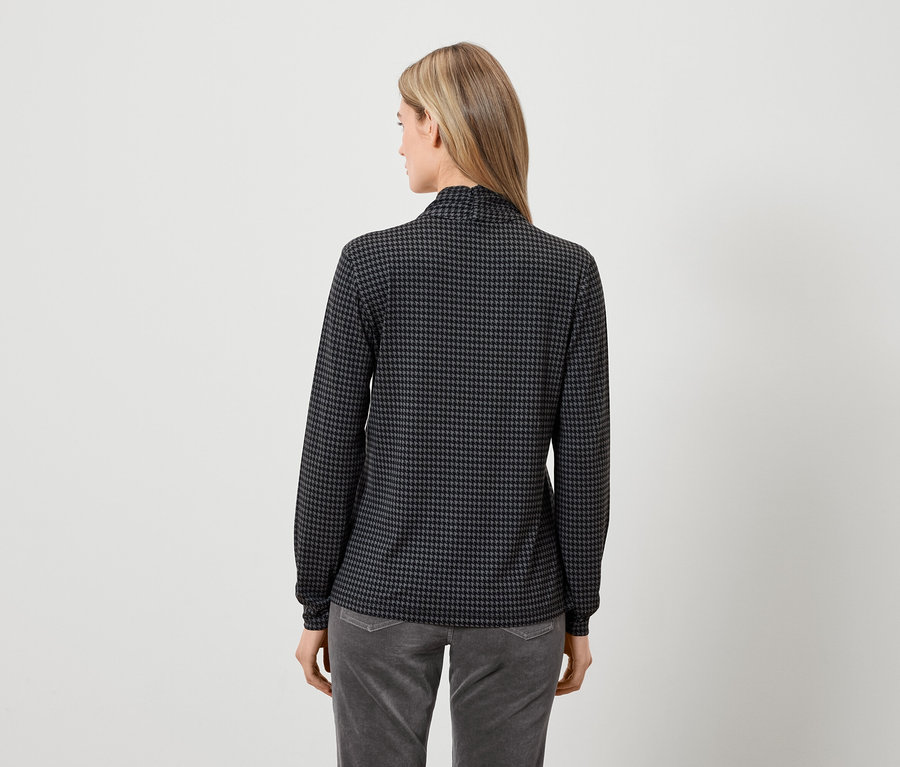 Rückansicht einer Frau in einem grau-schwarzen Langarmshirt und grauen Hosen.