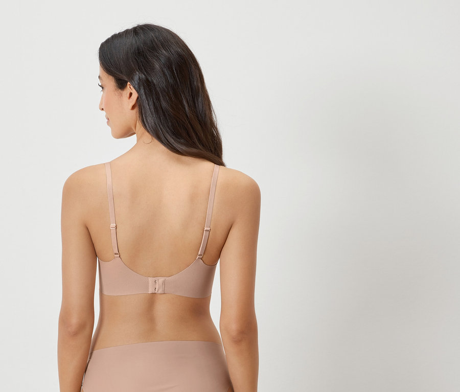 Rückansicht einer Frau mit dunklen Haaren, die einen hautfarbenen BH und ein passendes Höschen trägt.