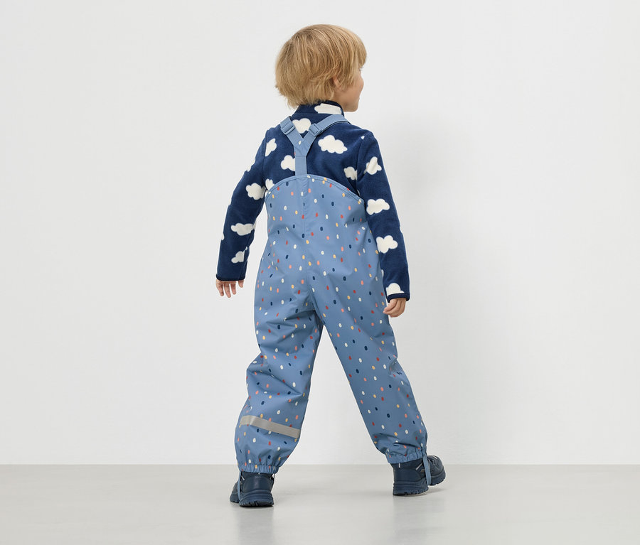 Kind von hinten, trägt blaue Matschhose mit bunten Punkten und Fleece-Pullover mit Wolken.