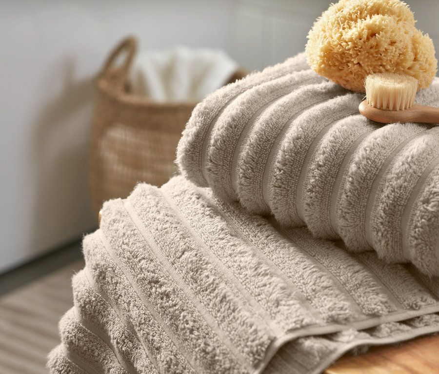 Zwei beige Premium-Handtücher mit Wellenstruktur liegen gestapelt mit einem Schwamm und einer Bürste auf einer Holzoberfläche.