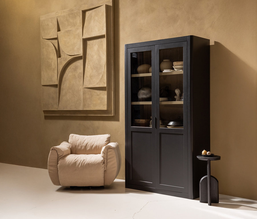 Dekoratives Interieur mit einem beigen Sessel, einem schwarzen Glasschrank und einem abstrakten Wandkunstwerk.