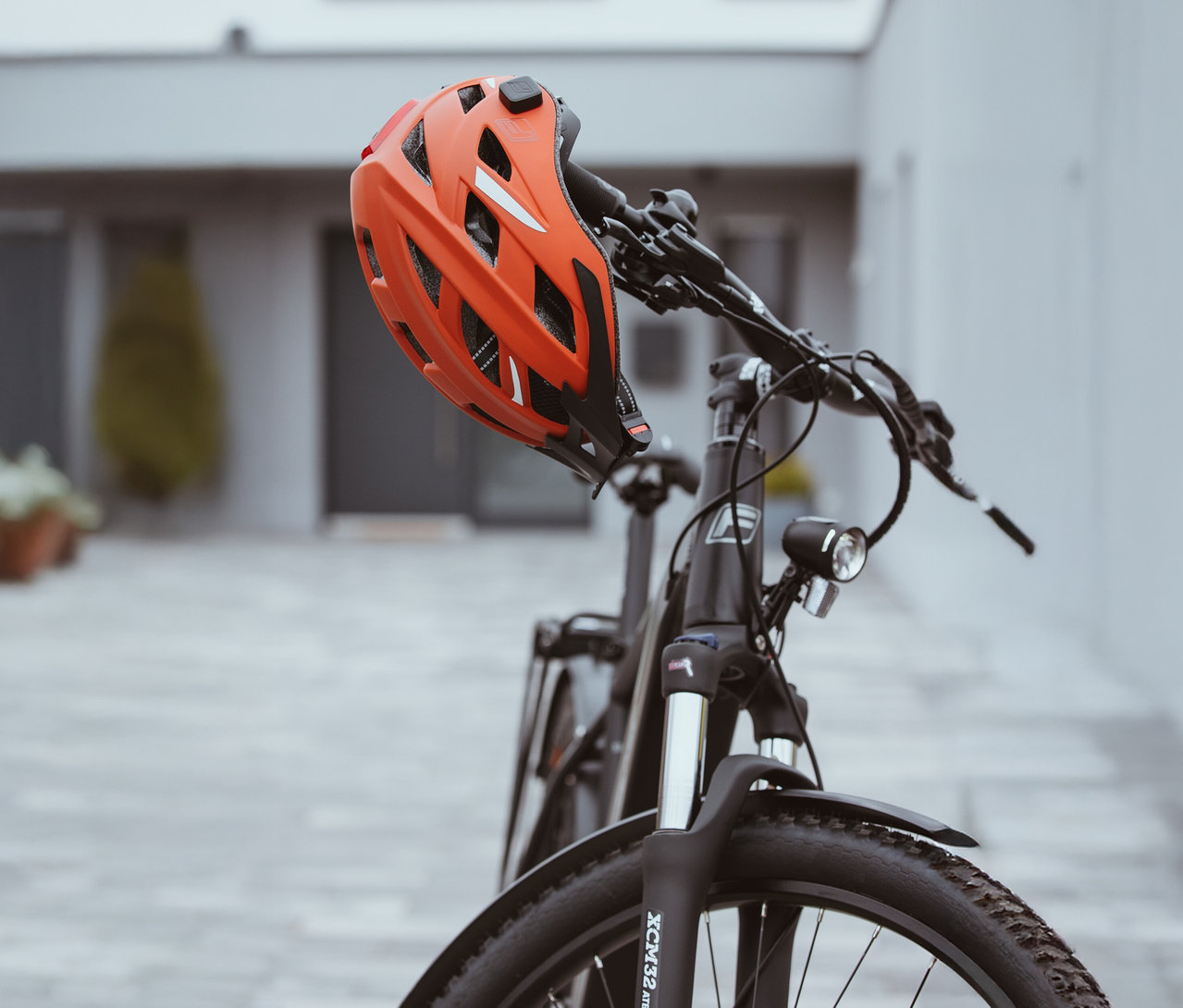 Ein orangefarbener FISCHER Fahrradhelm Urban PLUS Miami hängt am Lenker eines Fahrrads.