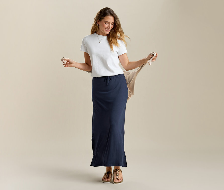 Frau hält beigen Cardigan und trägt ein weißes T-Shirt und einen langen Jerseyrock in Marineblau.