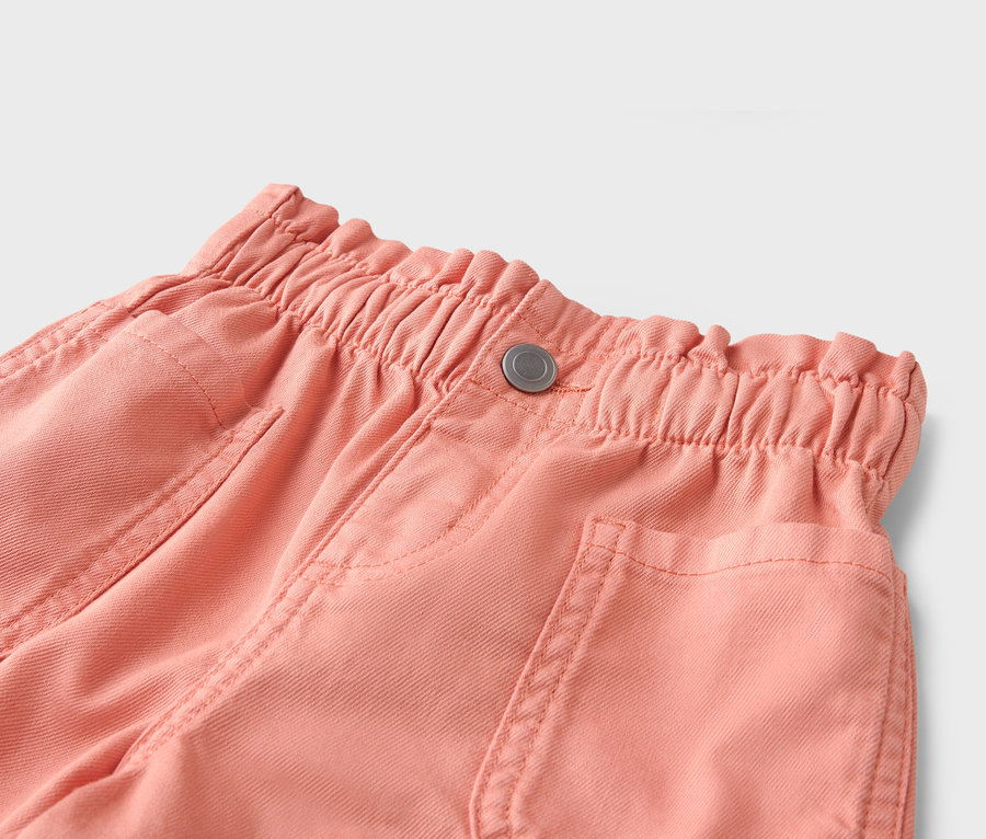 Nahaufnahme von korallenroten Hosen mit elastischem Bund und Knopf.