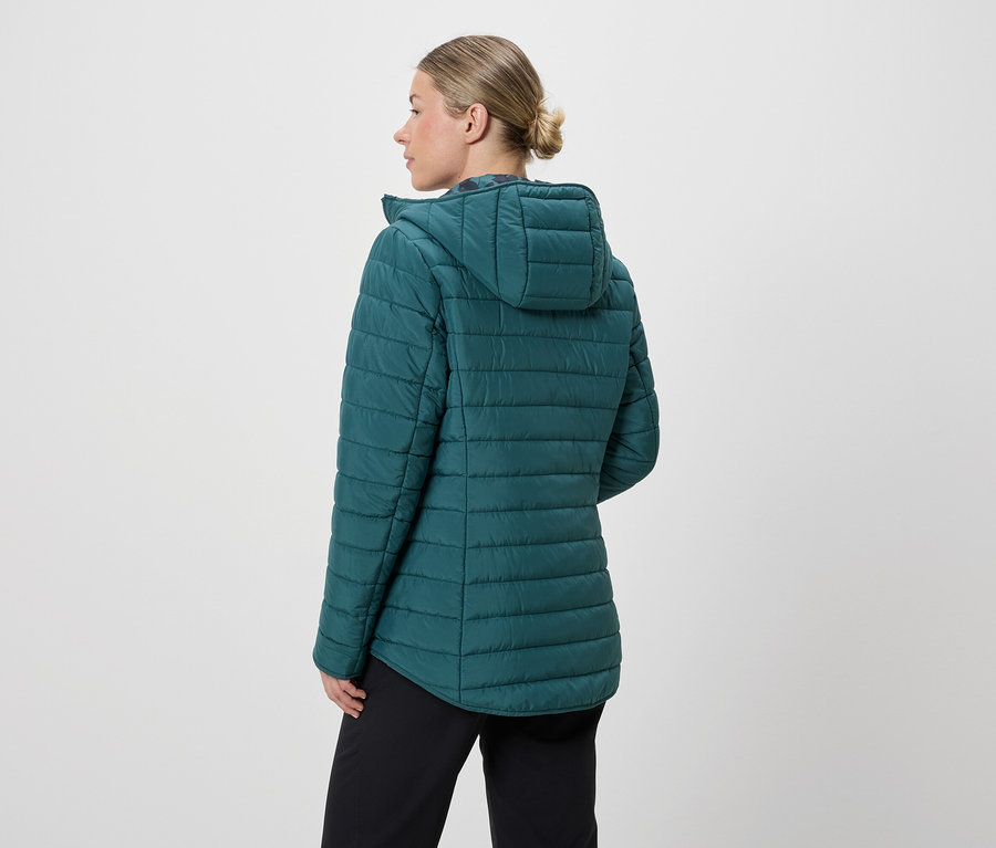 Eine Frau von hinten, mit Dutt, trägt eine petrolfarbene Steppjacke mit Kapuze und schwarze Hose vor einem weißen Hintergrund.