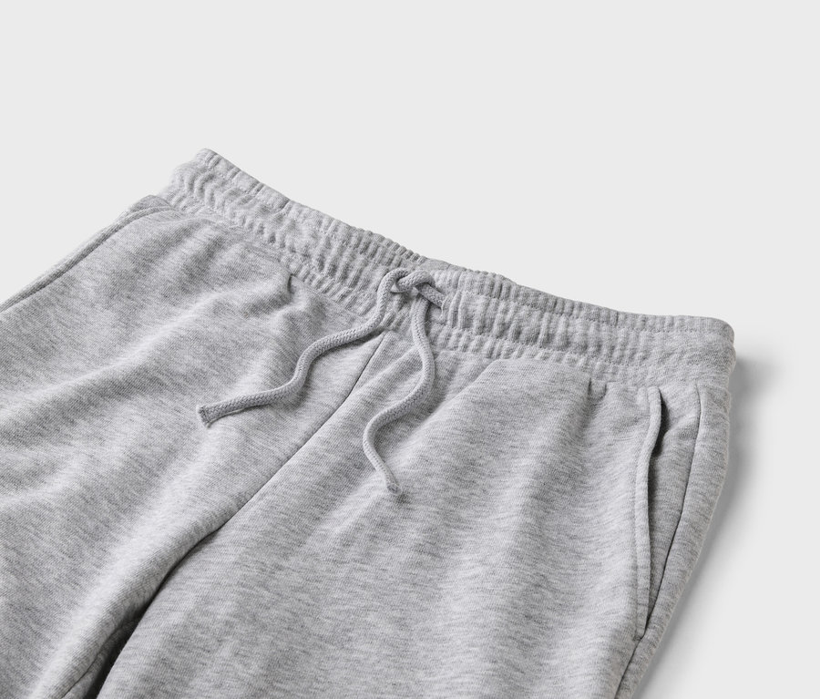 Nahaufnahme einer grauen Jogginghose mit Kordelzug und Taschen auf hellgrauem Hintergrund.