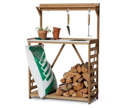 Ein hölzerner Gartentisch mit Pflanzgefäßen, Werkzeugen, einem Sack Erde und Holzscheiten.