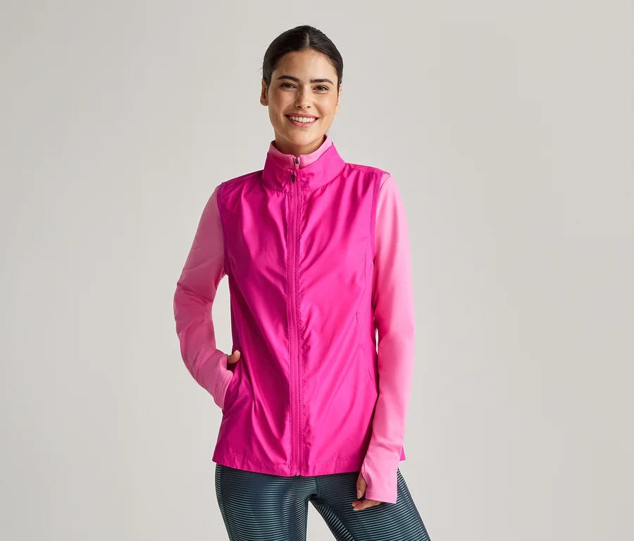Lächelnde Frau mit pinker Weste über einem pinken Langarmshirt und Leggings mit Streifen.