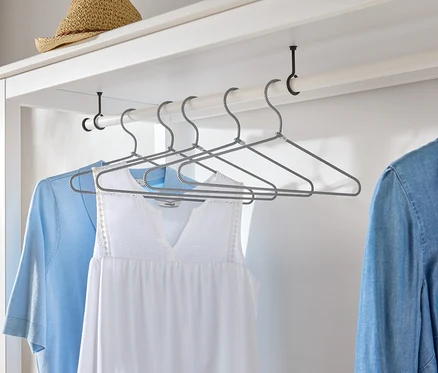 Kleidungsstücke hängen an Kleiderbügeln in einem weißen Kleiderschrank.