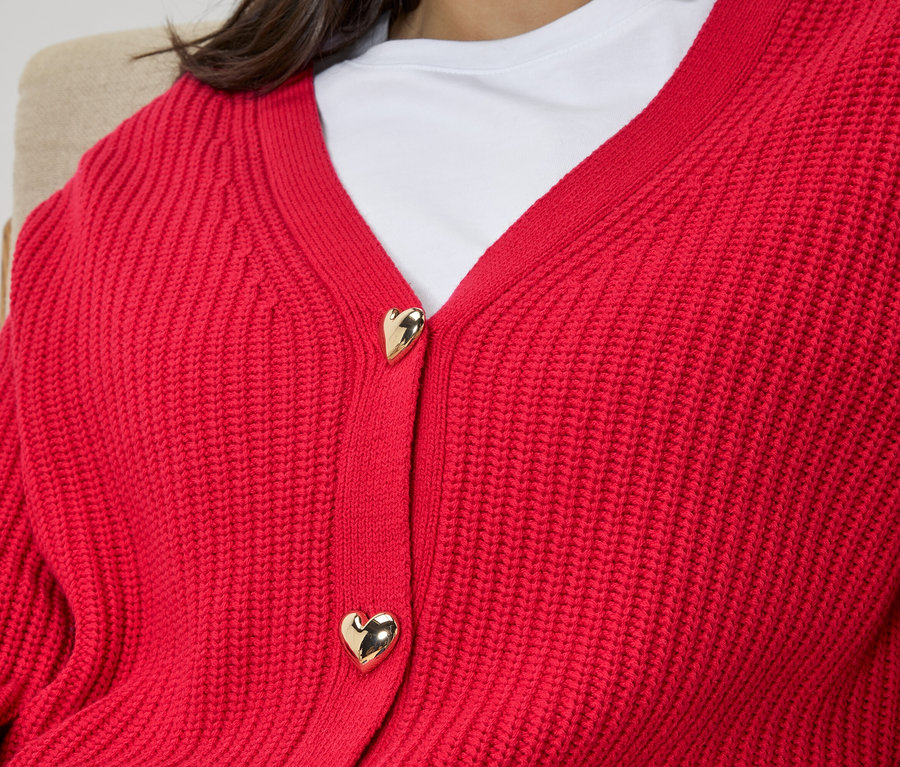 Nahaufnahme einer Frau, die einen roten Strickcardigan mit goldenen, herzförmigen Knöpfen trägt.