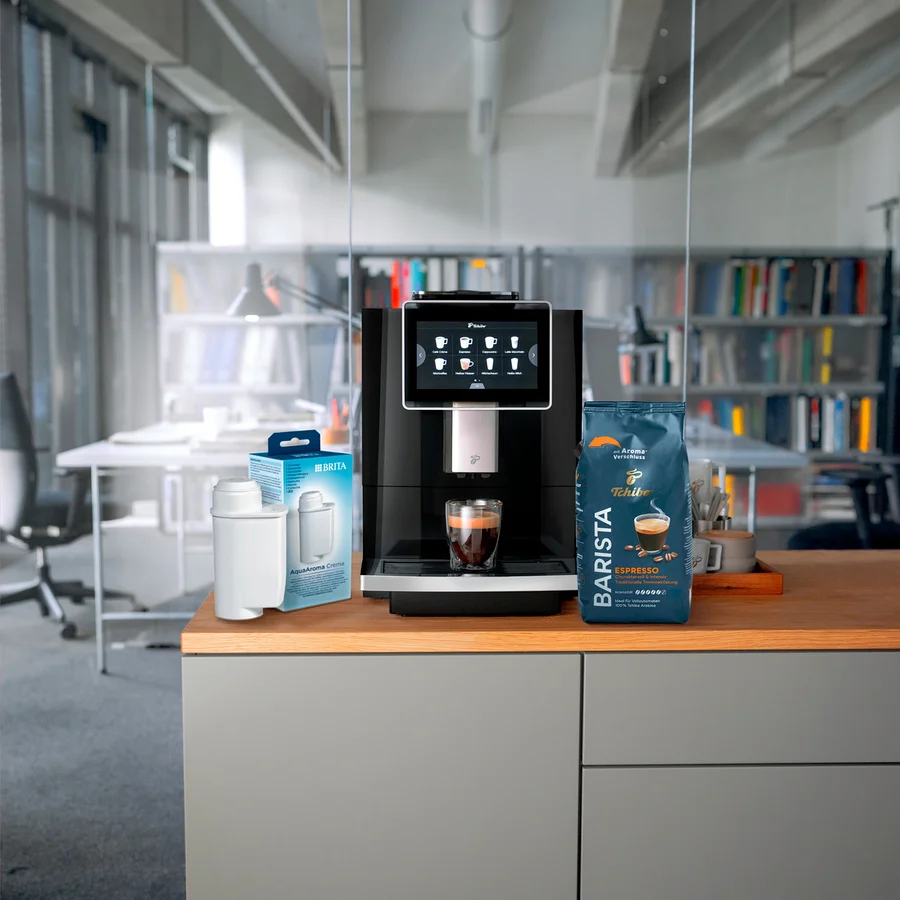 Auf einer Küchentheke stehen eine Kaffeemaschine, eine Packung Brita Wasserfilter und eine Packung Tchibo Barista Espresso.