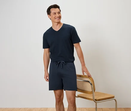 Ein Mann steht neben einem Stuhl und trägt ein marineblaues T-Shirt und Shorts.