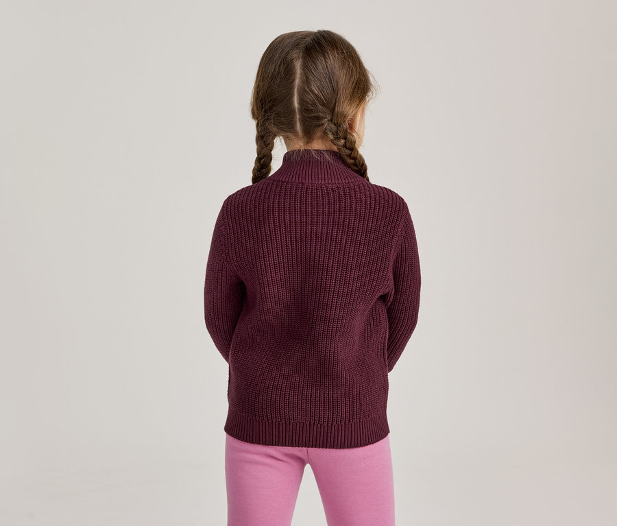 Mädchen von hinten gesehen, trägt einen burgunderroten Strickpullover und pinke Leggings, die Haare sind zu zwei Zöpfen geflochten.