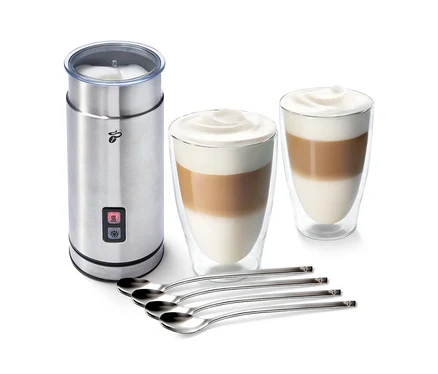Ein Edelstahl-Milchaufschäumer neben zwei Gläsern mit Kaffee und Milchschaum und vier Löffeln. Zu sehen ist das Milchschäum-Set "Cremige Versuchung".