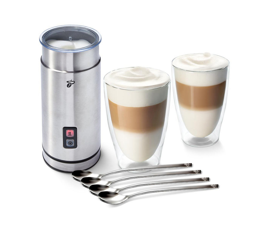 Ein Edelstahl-Milchaufschäumer neben zwei Gläsern mit Kaffee und Milchschaum und vier Löffeln. Zu sehen ist das Milchschäum-Set "Cremige Versuchung".