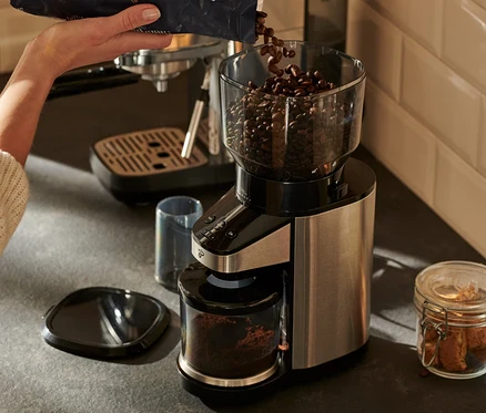 Frau schüttet Kaffeebohnen in eine elektrische Kaffeemühle mit Waage.