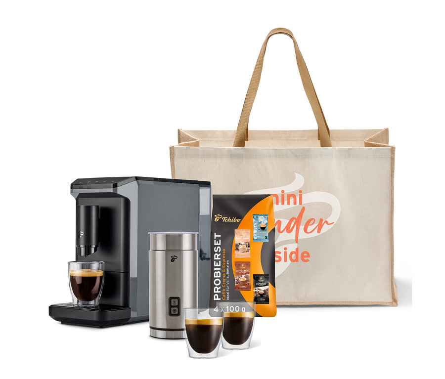Kaffeemaschine, Milchaufschäumer, zwei Tassen Kaffee und eine Tragetasche mit Aufschrift.