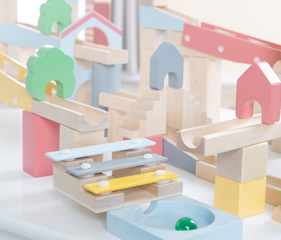 Ein pastellfarbenes Murmelbahn-Spielzeugset aus Holz mit Bahnen, Blöcken, Baum- und Hausformen und einem integrierten Xylophon. Eine grüne Murmel liegt in einer hellblauen Auffangschale.