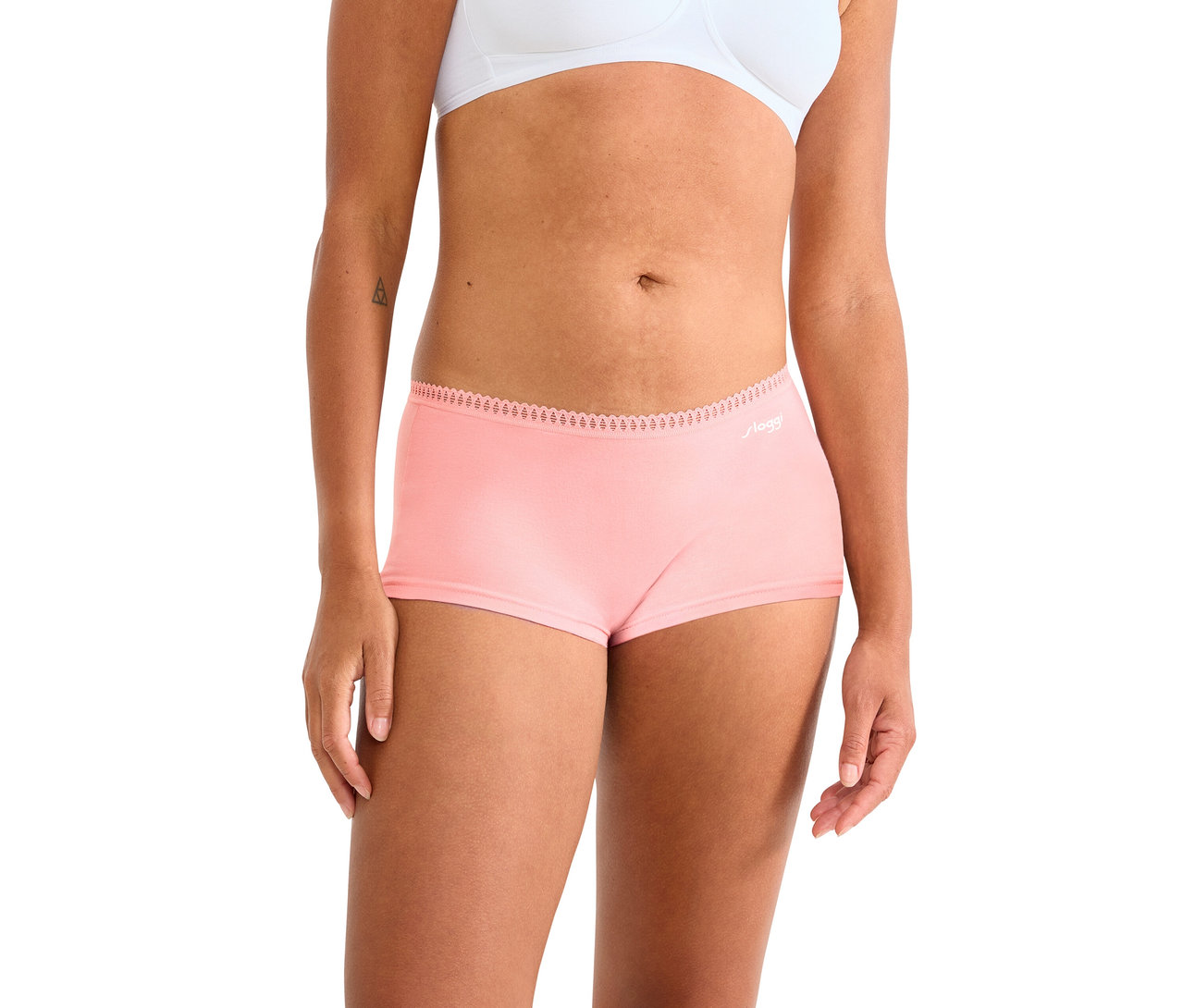 Oberkörper und Oberschenkel einer Frau, die einen weißen BH und rosa Boy-Shorts trägt. Die Boy-Shorts haben einen Spitzenbesatz am Bund und ein „sloggi“-Logo.