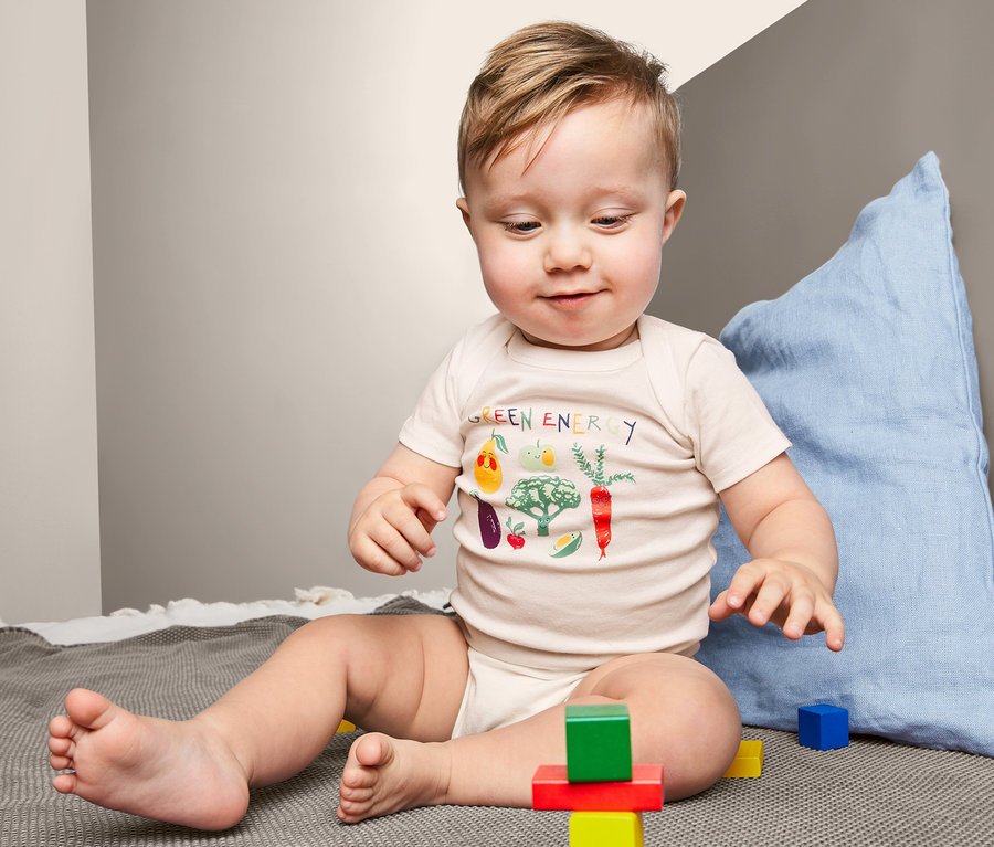 Baby sitzt auf einer Decke und spielt mit bunten Würfeln. Es trägt einen 3 Kurzarmbody mit Gemüseaufdruck.