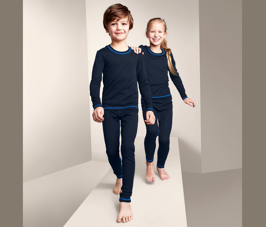 Zwei Kinder in marineblauer Funktionsunterwäsche mit blauen Bündchen gehen auf einer weißen Plattform.