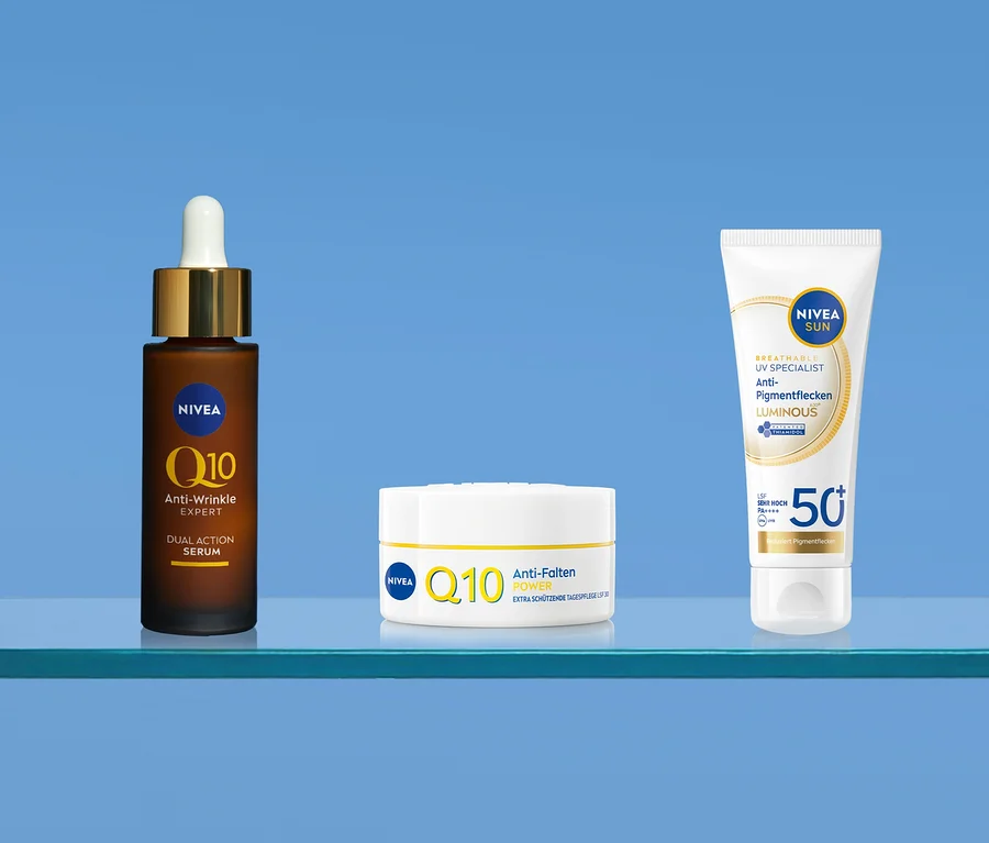 Drei Nivea Produkte auf einem blauen Regal: ein braunes Q10 Anti-Falten Expert Serum, eine weiße Q10 Anti-Falten Power Tagespflege und eine Nivea Sun UV Specialist Anti-Pigmentflecken Luminous SPF 50+ Sonnencreme.