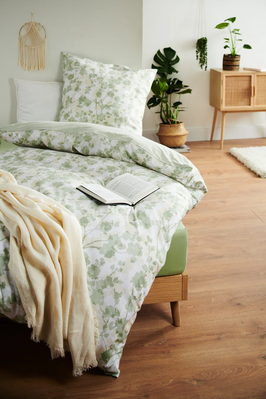 Bett mit blumiger Bettwäsche und offenem Buch. Renforcé-Bettwäsche in Übergröße und Normalgröße sind vorhanden.