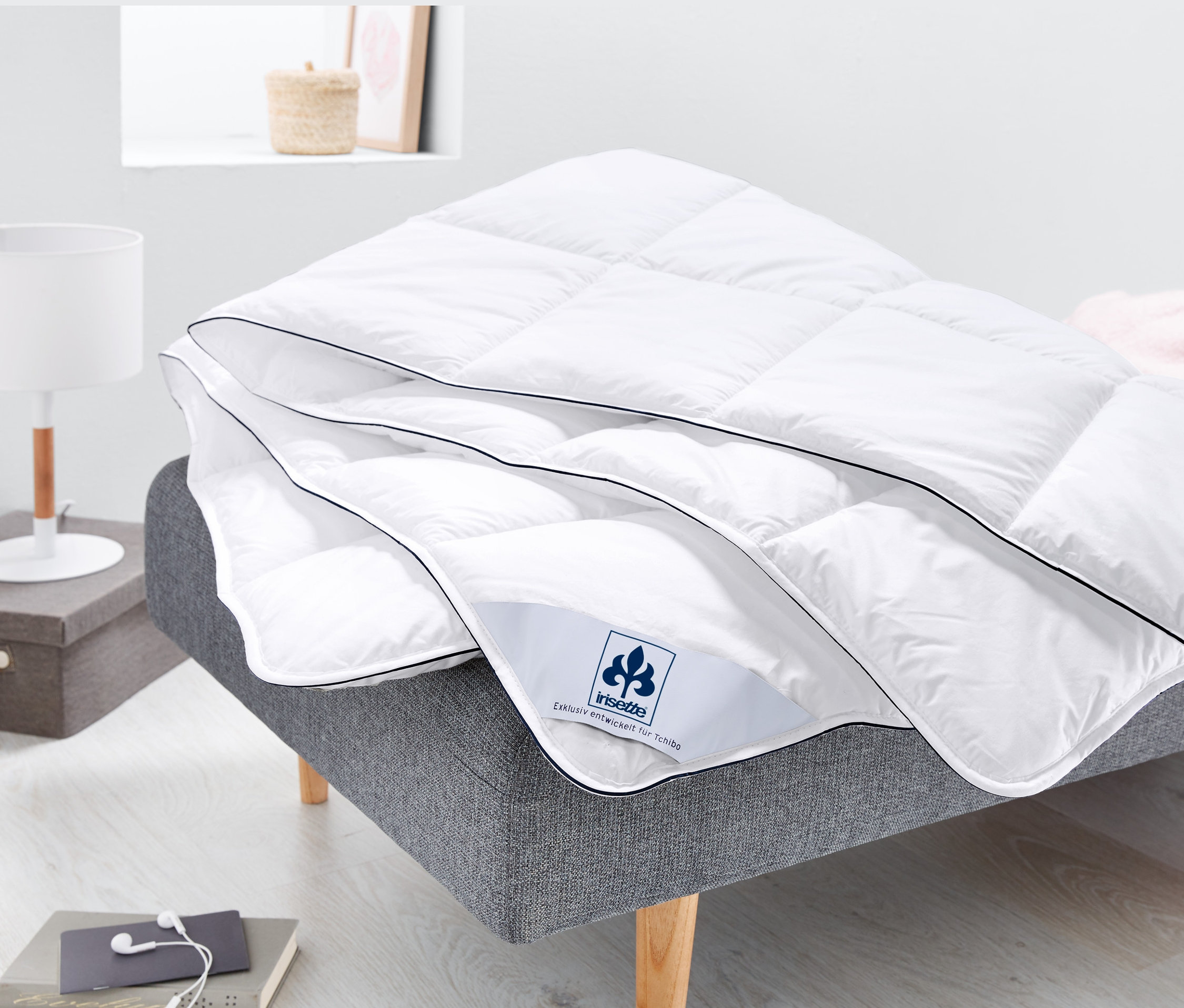 Ein weißes irisette®-Steppbett mit Faserfüllung liegt auf einem grauen Sofa.