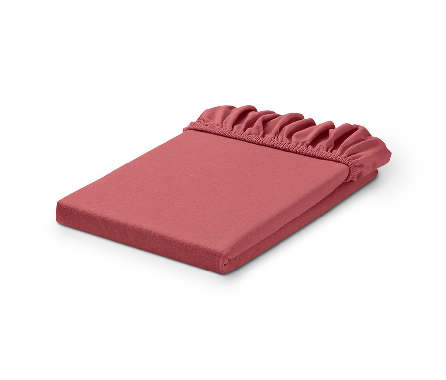 Ein gefaltetes, rosafarbenes Spannbetttuch mit Rüschen auf einem weißen Hintergrund.