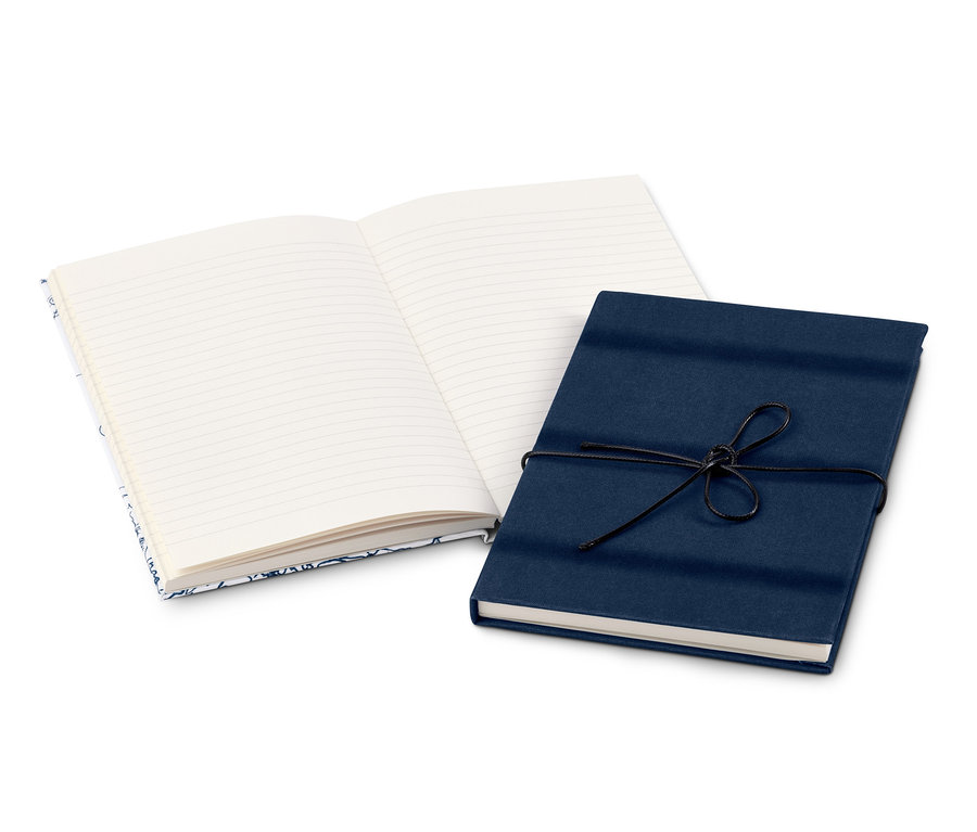 Zwei Notizbücher liegen auf einer weißen Oberfläche. Eines ist offen mit linierten Seiten, das andere ist geschlossen, mit dunkelblauem Papier umwickelt und mit einer schwarzen Schnur verschnürt.