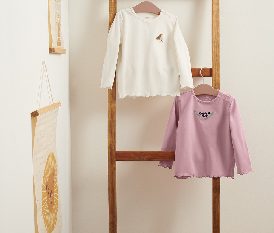 Zwei Langarmshirts hängen auf einer Holzleiter.