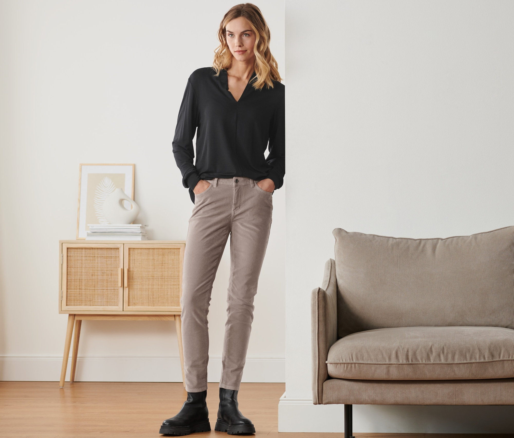 Frau steht mit Händen in den Taschen ihrer Samthose.