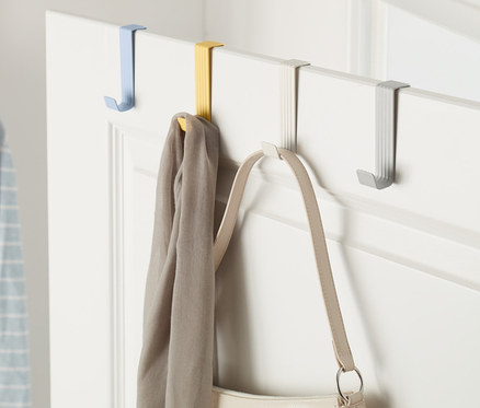 An einer Tür hängen 4 Türhaken in verschiedenen Farben, an denen ein Schal und eine Handtasche hängen.