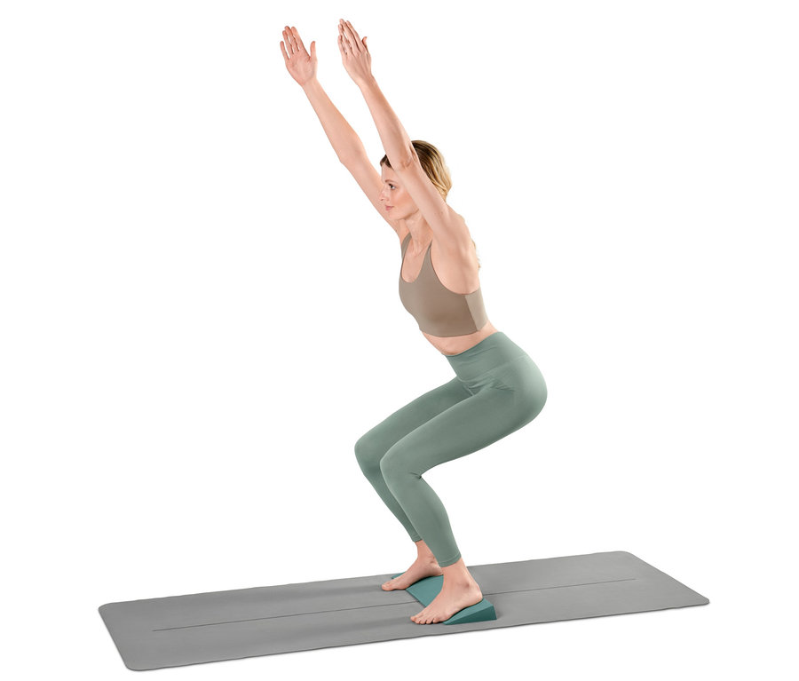 Frau macht Stuhl-Pose auf einer Yoga-Matte mit einem Yoga-Wedge unter ihren Fersen.