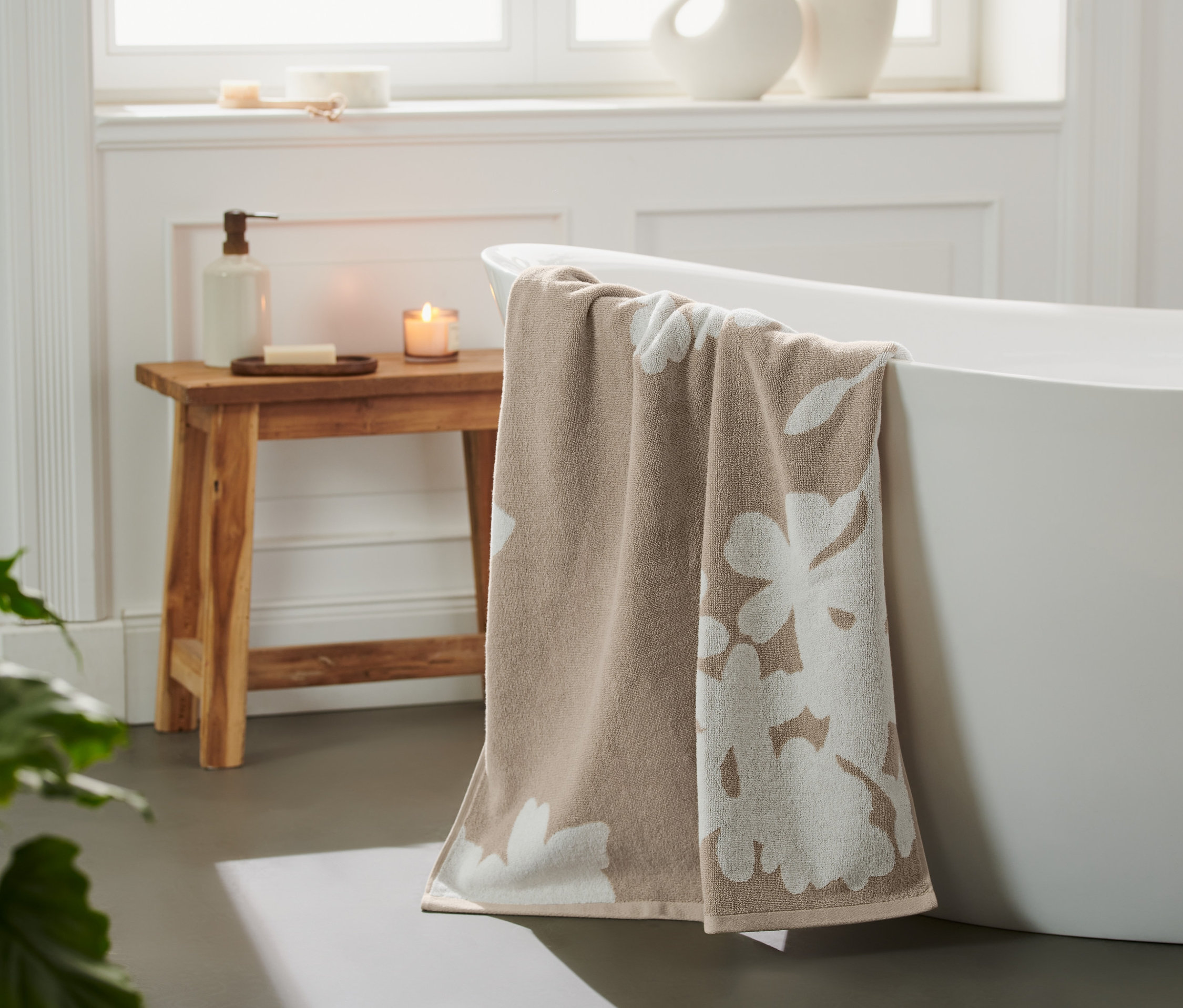 Beiges Jacquard-Badetuch mit Blumenmuster hängt über dem Rand einer weißen Badewanne.