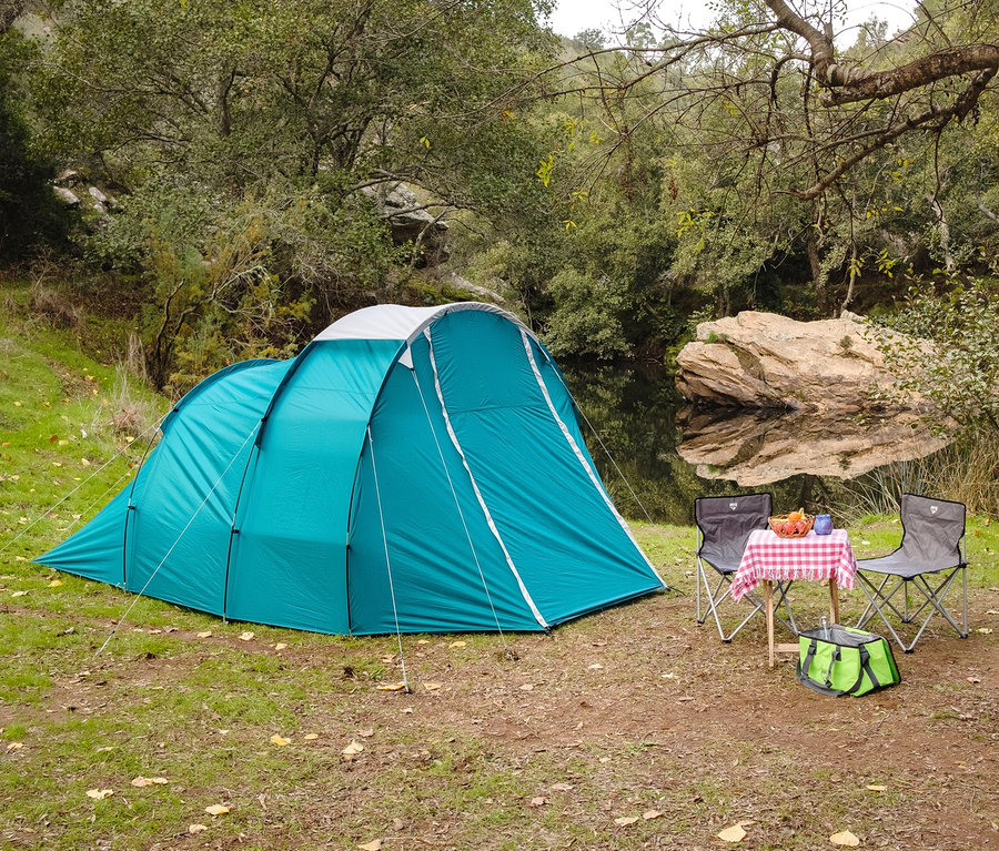 Ein türkisfarbenes Pavillo™ Zelt »Family Dome 4« steht auf einer Wiese neben einem Fluss.