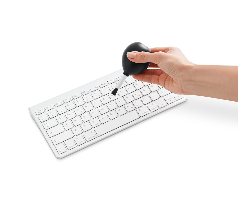 Eine Hand reinigt eine weiße Tastatur mit einer 2-in-1-Blowerbürste.