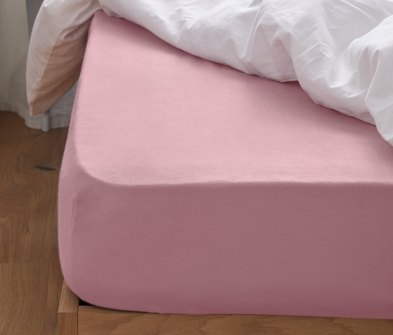 Rosa Biber-Spannbettlaken auf einem Bett mit weißer Bettdecke und rosa Kissen.