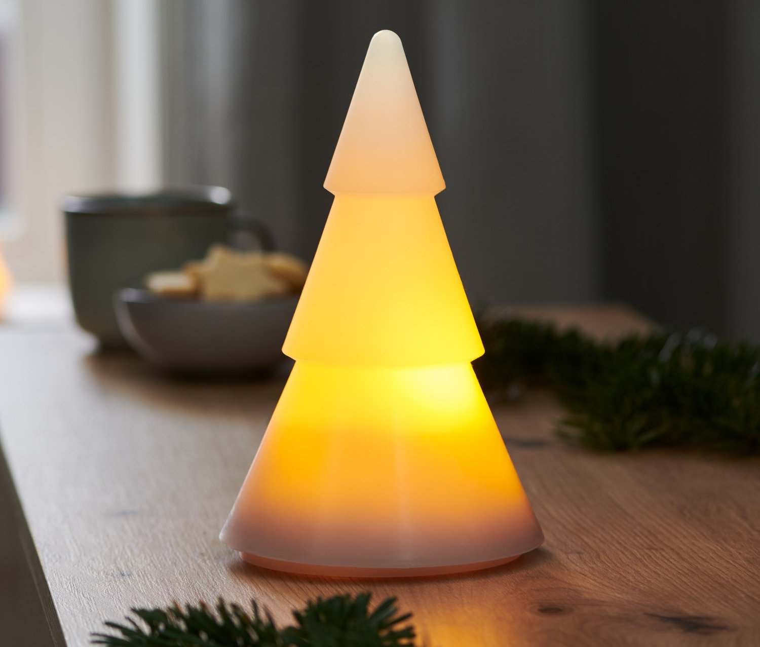 Eine LED-Echtwachstanne steht auf einem Tisch. Im Hintergrund ist ein Fenster.