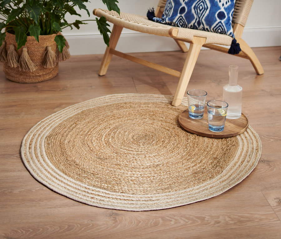 Ein runder Jute-Teppich mit cremefarbenem Rand liegt auf einem Holzboden.