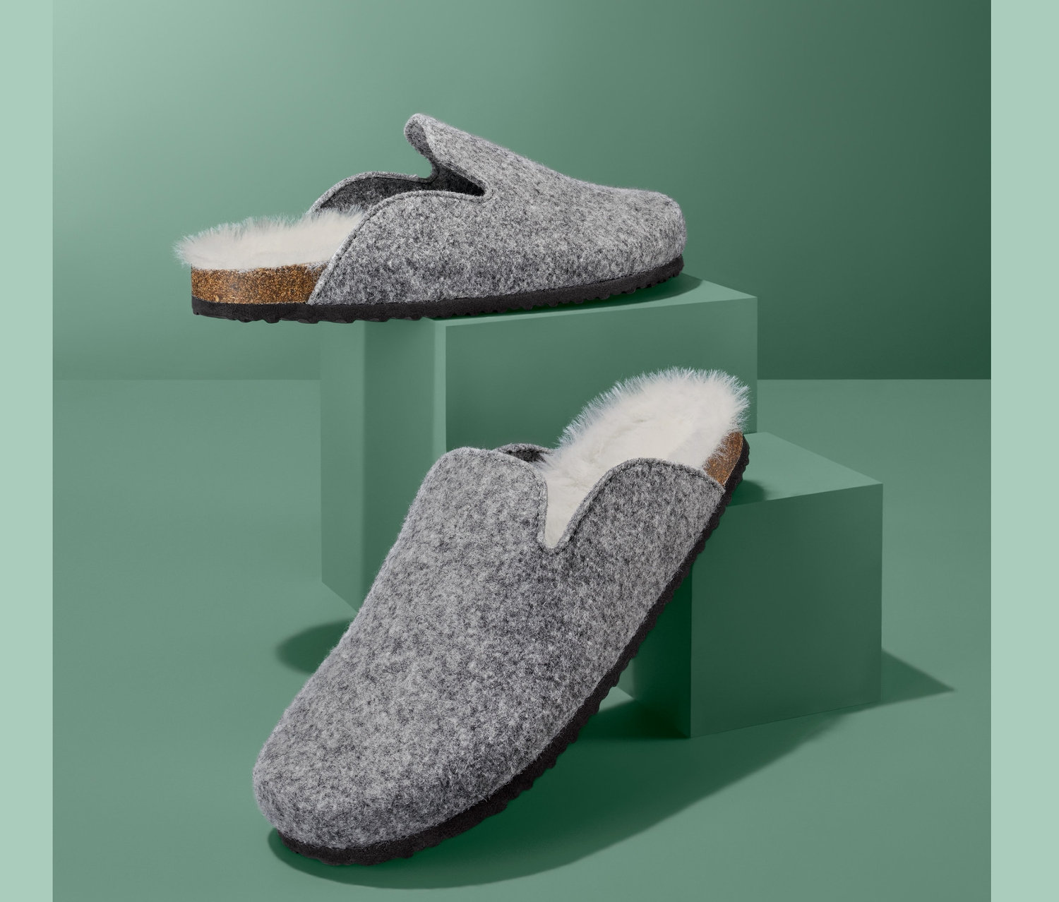 Zwei graue Hausschuhe auf grünen Sockeln.