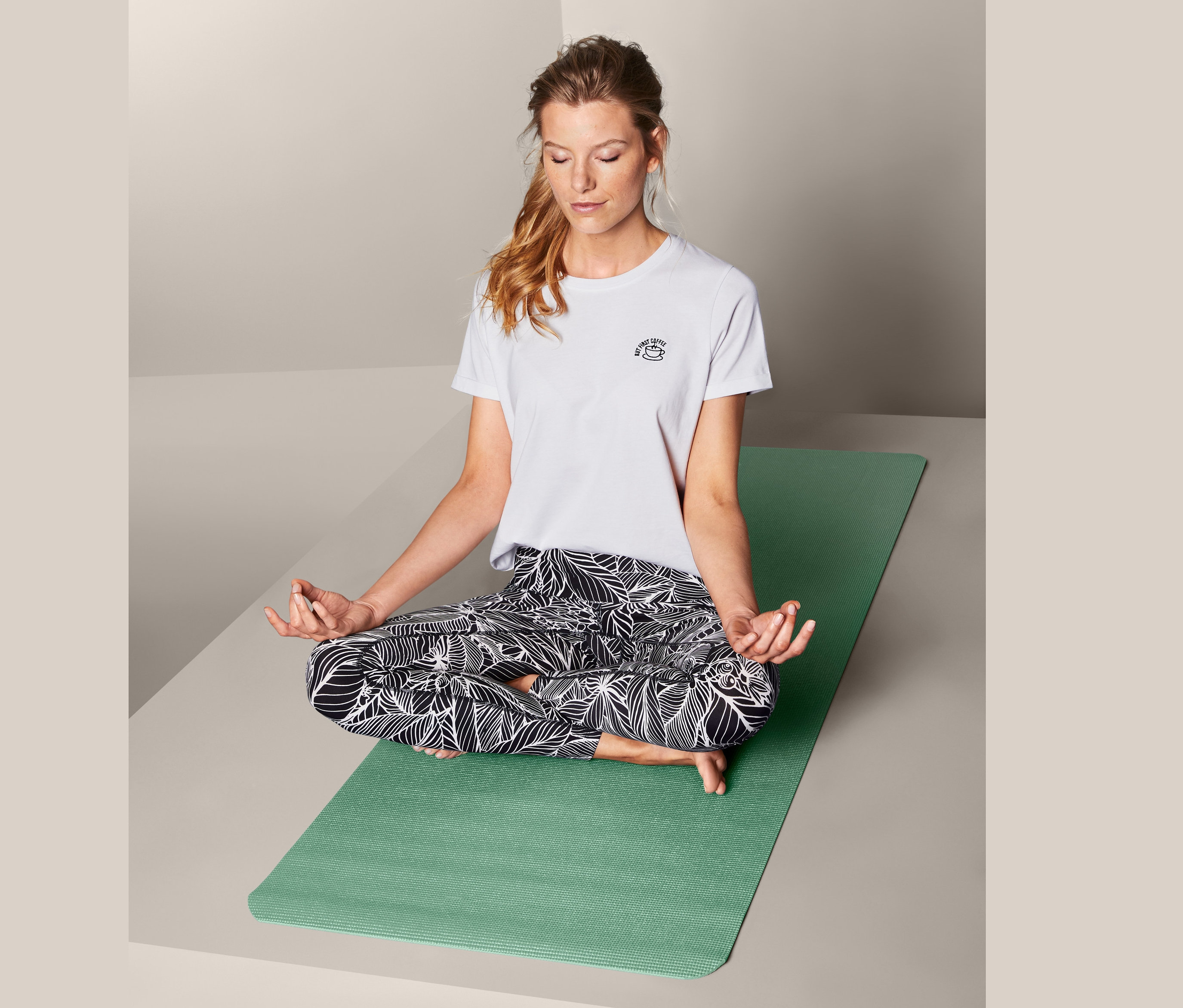 Frau sitzt im Schneidersitz auf einer Yoga- und Fitnessmatte.