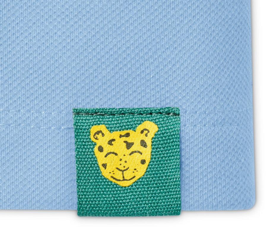 Detailaufnahme eines hellblauen Poloshirts mit einem kleinen, grünen Aufnäher, der einen gelben Tigerkopf zeigt.