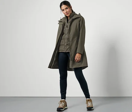 Eine Frau posiert in einem 3-in-1-Regenmantel mit Weste, dunklen Jeans und Wanderstiefeln.