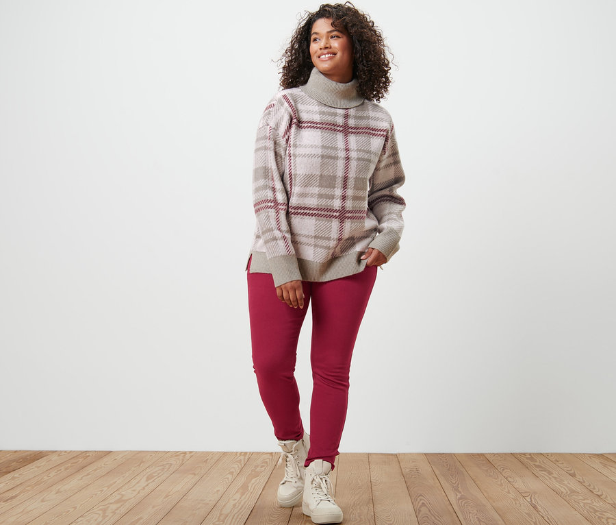 Eine Frau steht und trägt einen Strickpullover mit Rollkragen und Jeggings.