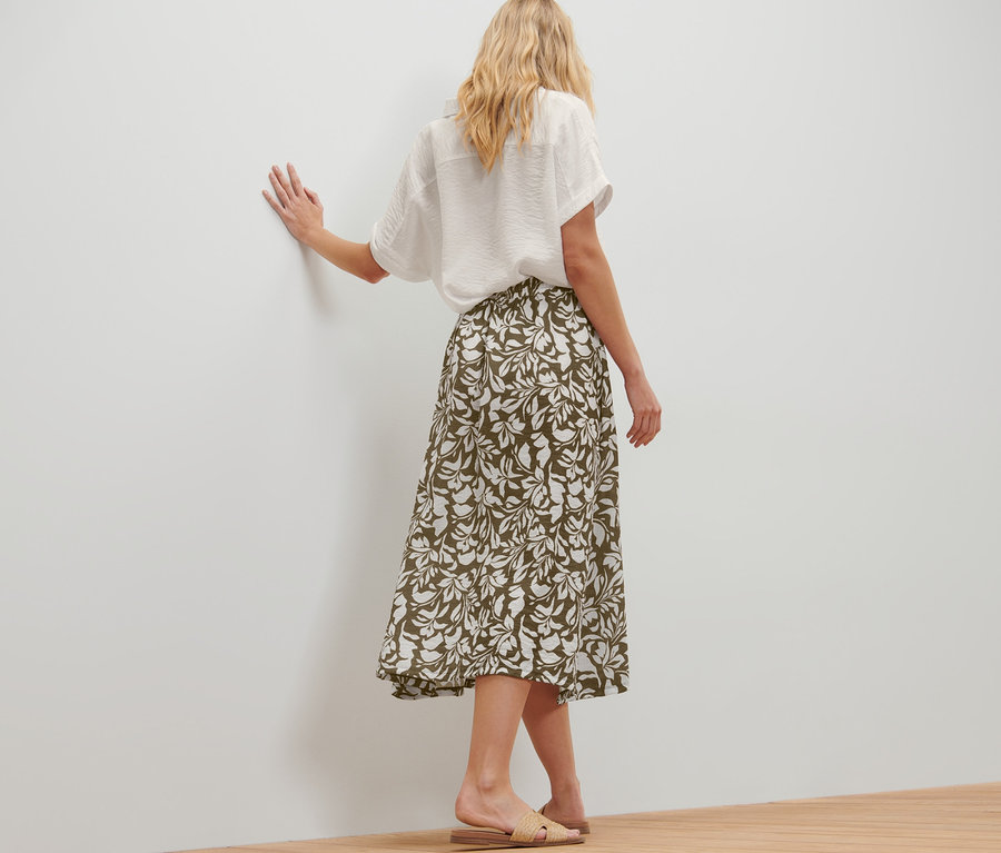 Frau posiert in bedrucktem Midirock und weißem Hemd.