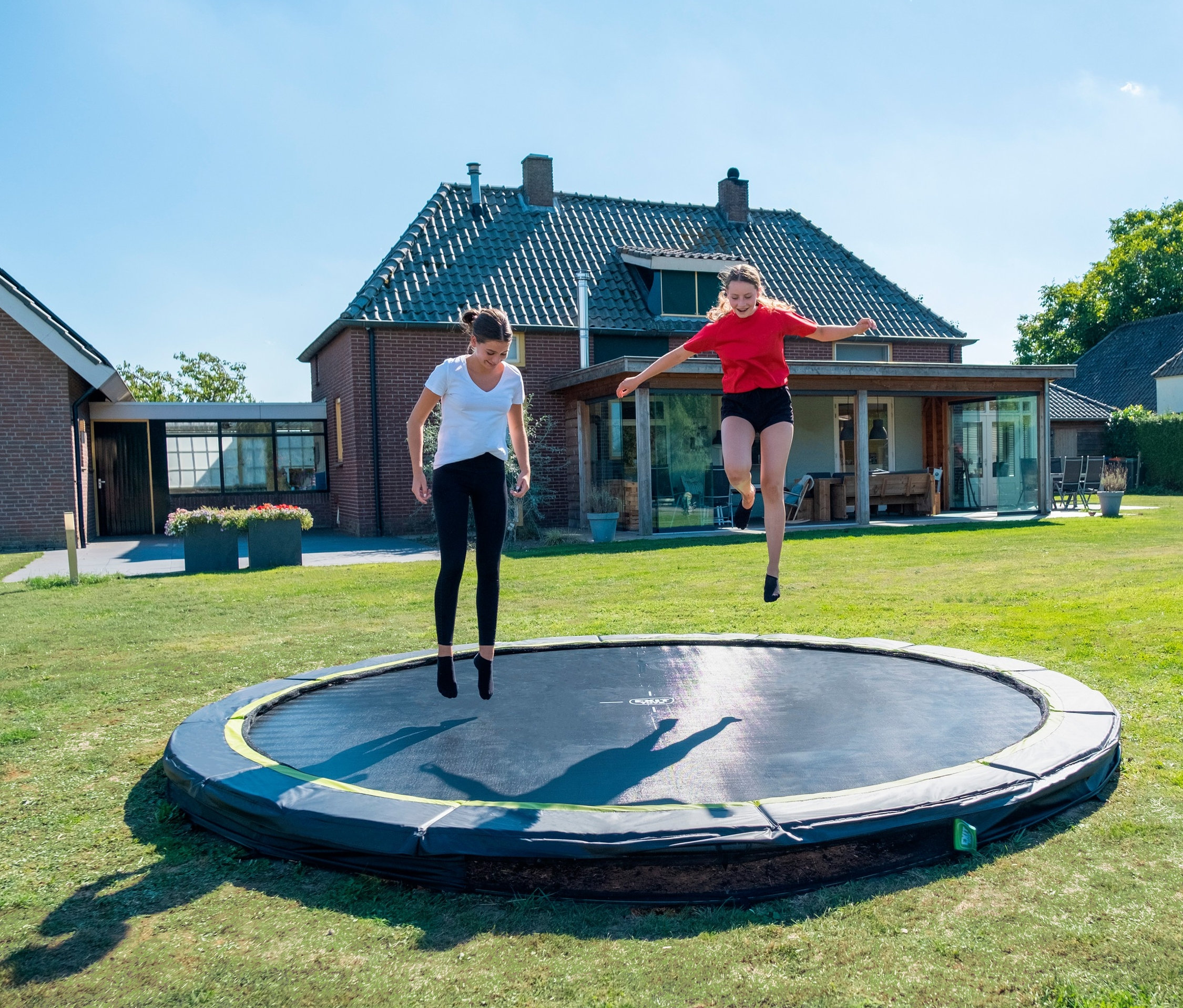 Zwei Mädchen springen auf einem EXIT Bodentrampolin »Silhouette sports« mit ca. 427 cm Durchmesser auf einer Wiese.