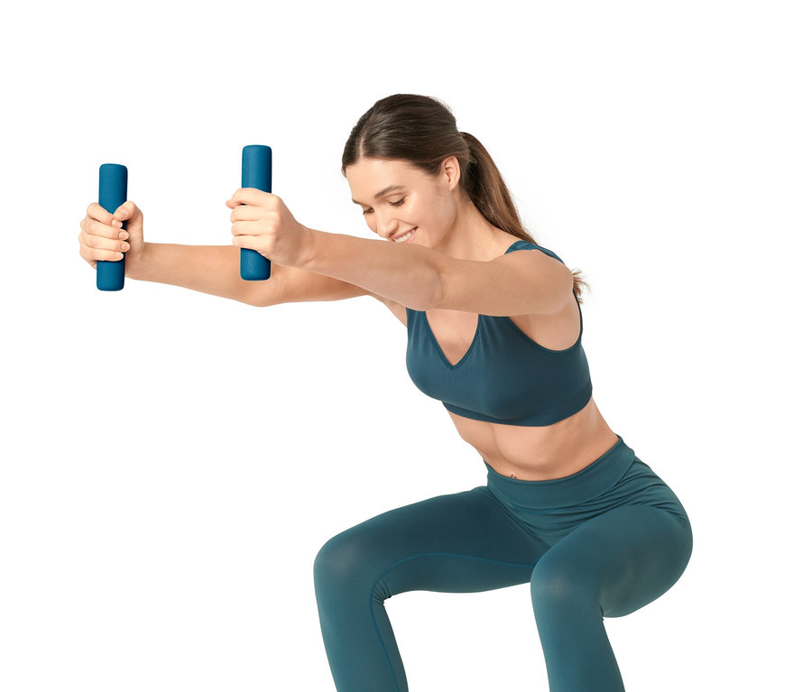 Frau macht Kniebeugen mit 2 blauen Hanteln in den Händen.