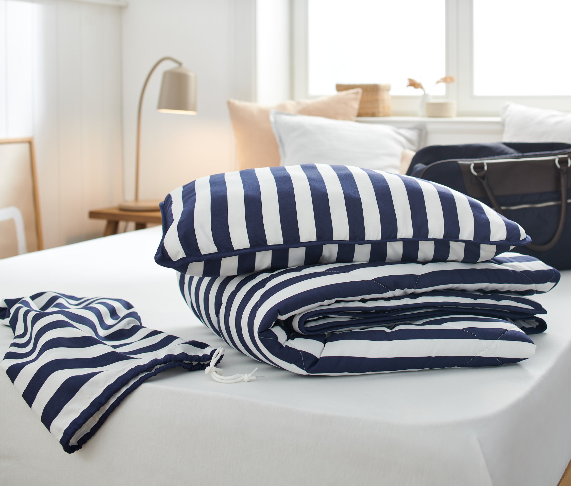 Ein Reise-Bettenset mit blau-weissen Streifen liegt auf einem weißen Bett.