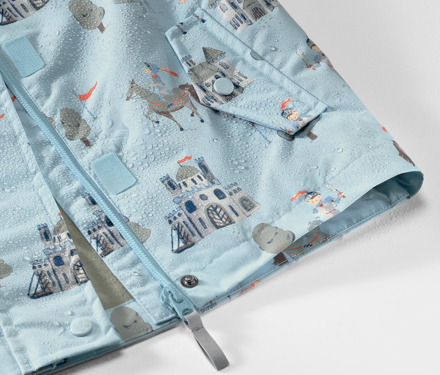Detailansicht einer Kinder-Regenjacke mit Rittermuster, auf der Wassertropfen zu sehen sind.